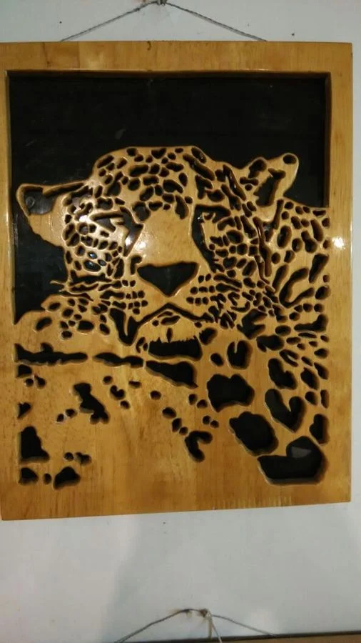 Resting leopard hand-cut in wood over a dark backing