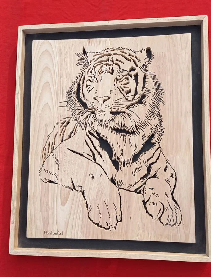 Seated tiger hand-cut in wood, framed and shown on a red ground